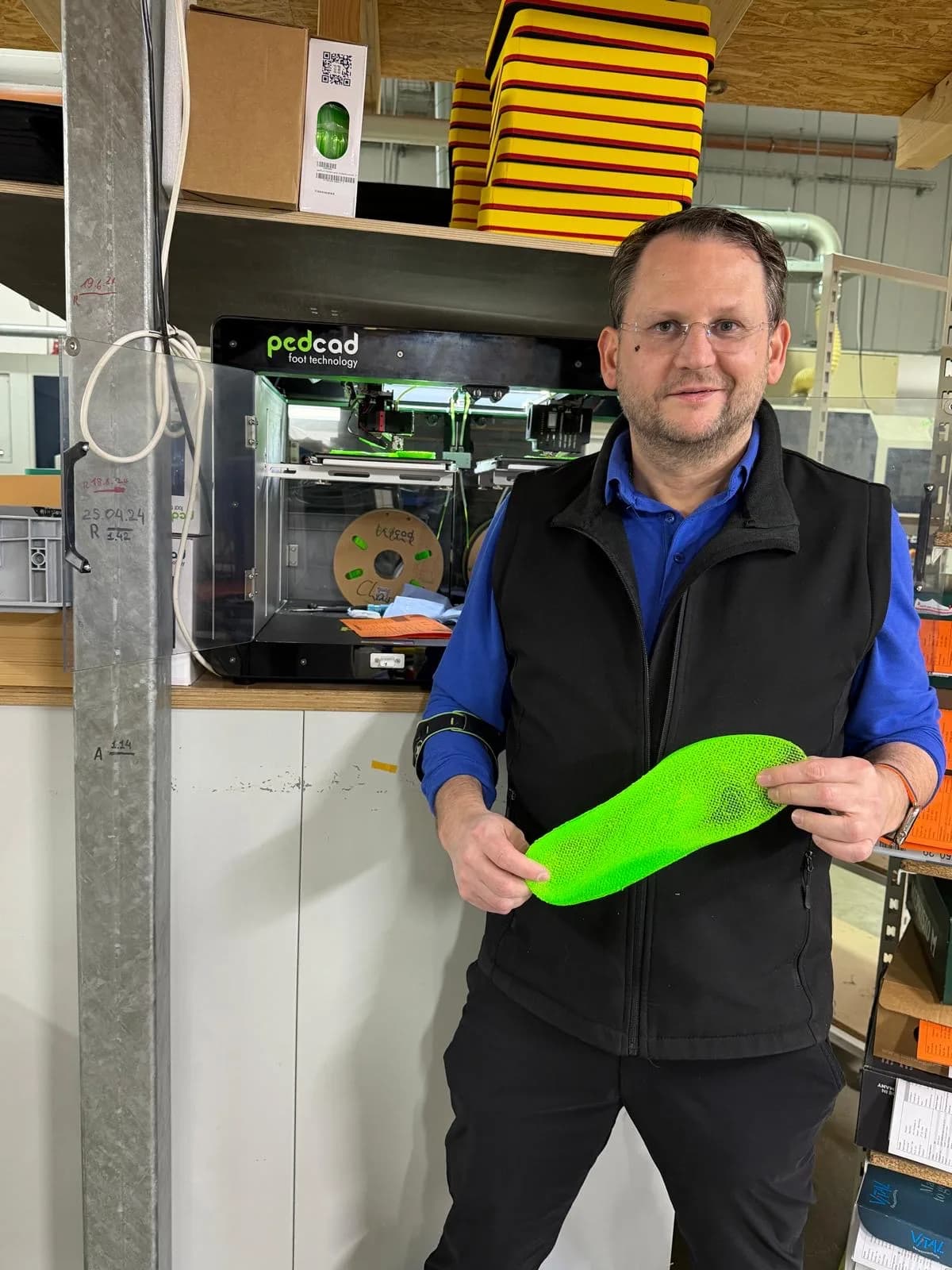 Helmut Wurzlbauer hält eine 3D-gedruckte Einlage vor dem 3D-Drucker in der Werkstatt